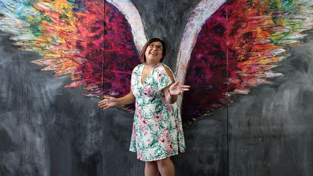  凡妮莎·麦卡伦在一幅绘有天使翅膀的彩色壁画前摆姿势.