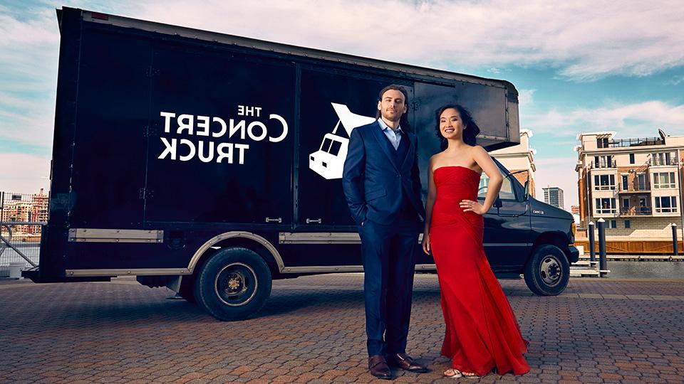 a woman in a red dress and a man in a suit stand in front of a black truck with the words the concert truck on it
